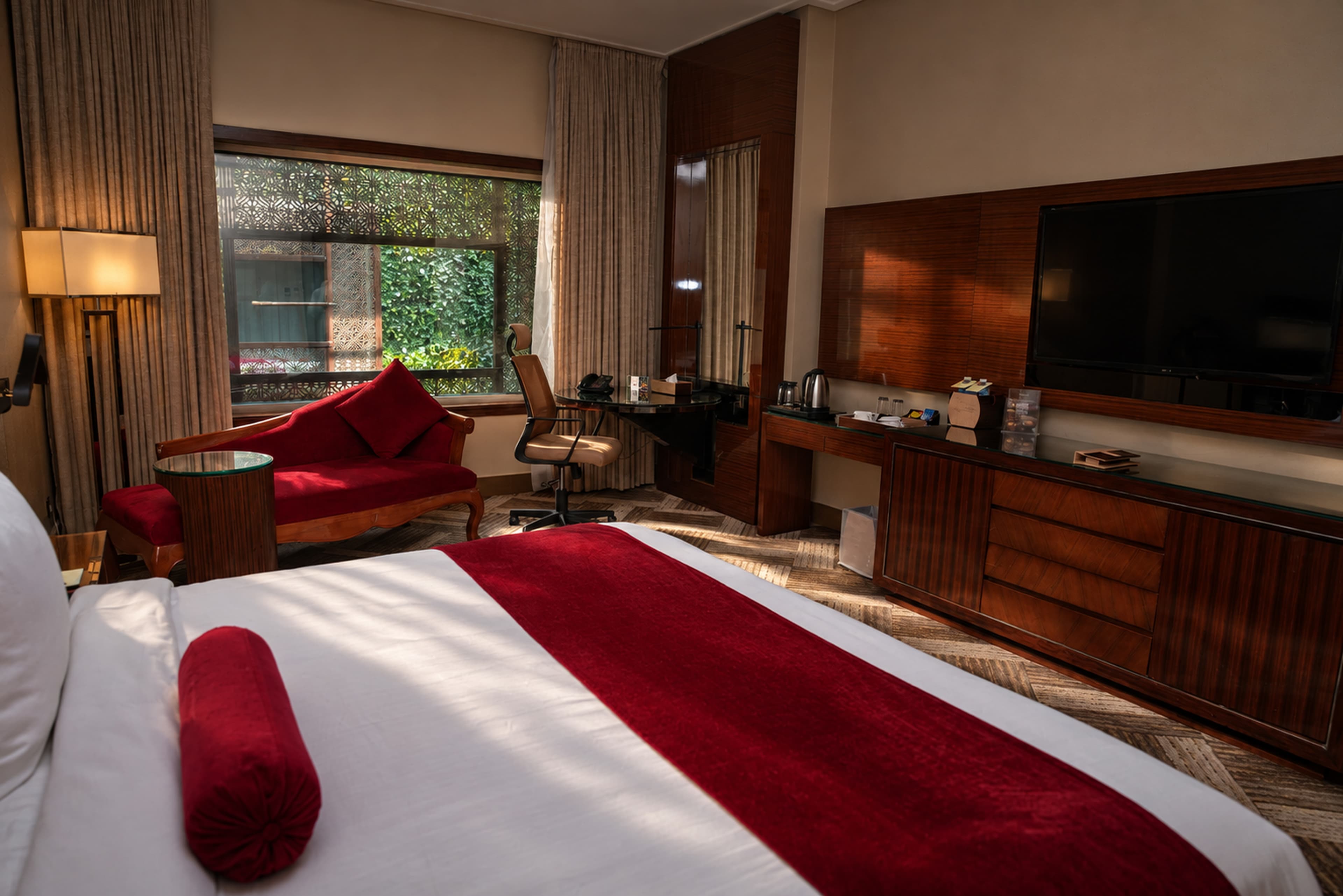 An Executive Room at Royal Swiss Lahore, with a work desk and red velvet chaise